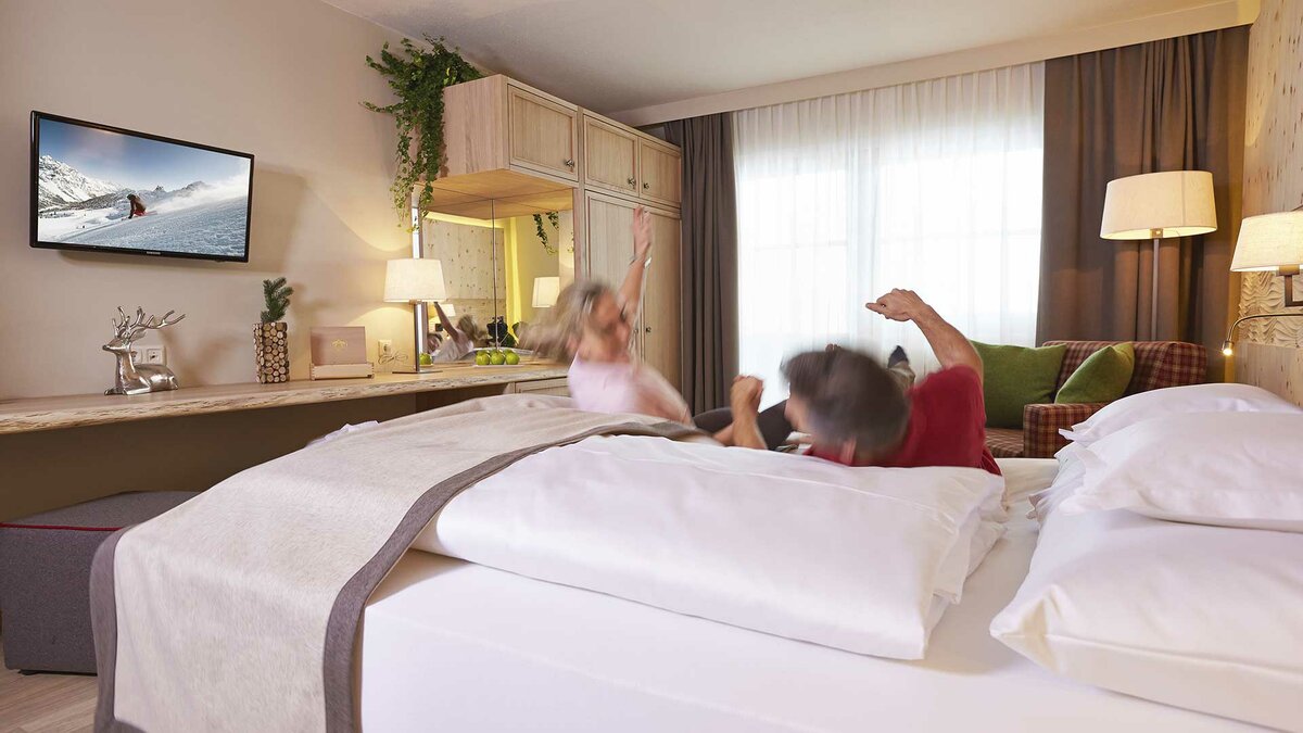 Ein Pärchen, das sich glücklich auf ein Bett fallen lässt in einem Doppelzimmer des Alpeiner Nature Resorts 
