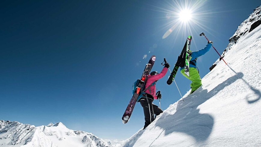 Zwei Skifahrer laufen einen verschneiten Berg nach oben. 