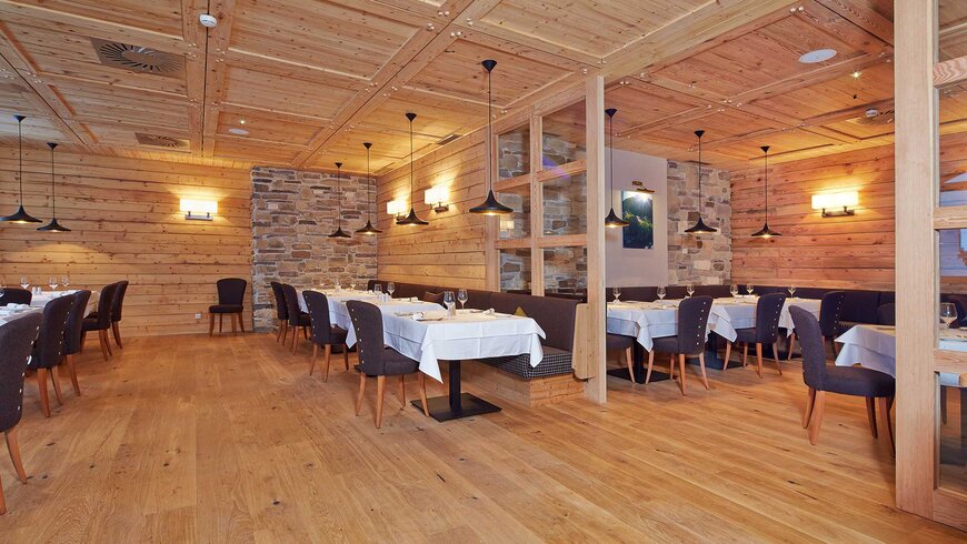 Holzgetäfeltes Restaurant mit Steinakzenten an den Wänden, elegant gedeckten Tischen und modernen Pendelleuchten.