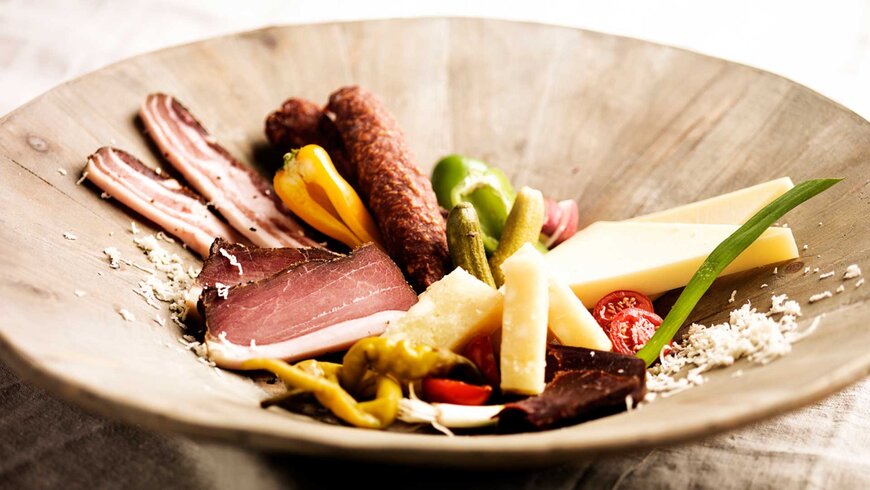 Bild einer Brettjause mit frischem Hartkäse, Räucherschinken und Gemüse. 