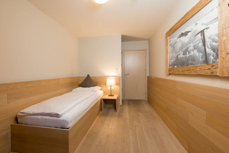 Ein einfaches Einzelzimmer verkleidet mit einem hellen Holz. 