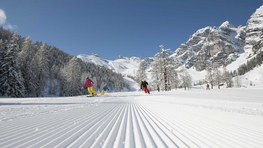 Drei Skifahrer fahren während des Aktivurlaubs in Tirol auf einer frischen Skipiste, im Hintergrund das verschneite Bergpanorama.