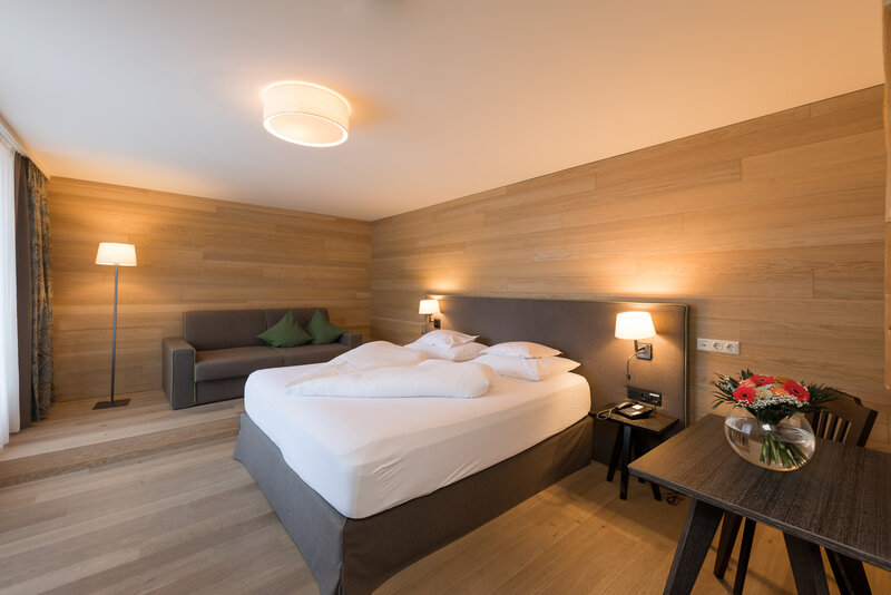 Gemütliches Hotelzimmer mit Doppelbett, Nachttischen und moderner Beleuchtung, ausgestattet mit Holzverkleidung und stilvollen Dekorationselementen.