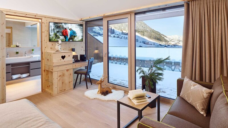 Einblick in den Wohnbereich eines lichtdurchfluteten, gemütlichen Hotelzimmers mit großem Balkon und Blick auf das Stubaital