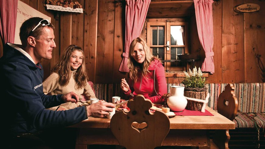 "Eine Familie sitzt an einem rustikalen Holztisch in einer gemütlichen Berghütte und genießt eine Mahlzeit.        "