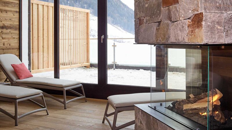 Ein Ruheraum im NatureSpa mit Liegen, Kamin und bodentiefen Fenstern mit Blick auf das Stubaital