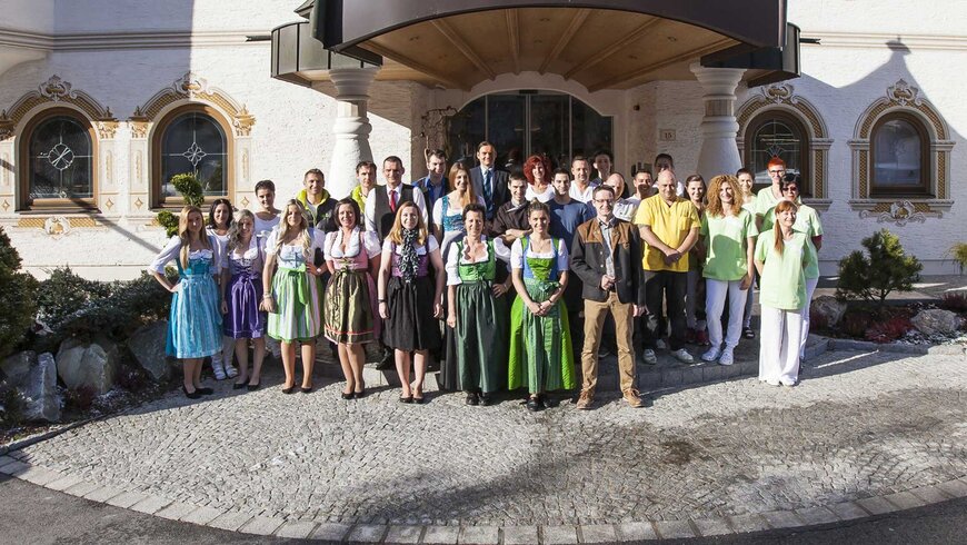 Das Personal des Nature Resort in Tirol posiert in traditioneller Tracht und moderner Kleidung vor dem Resort-Eingang.
