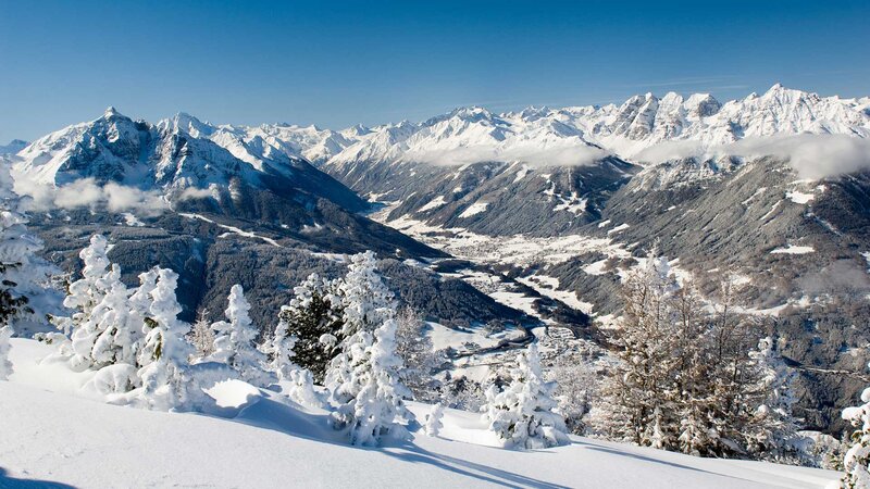 Winterlandschaft in Tirol mit schneebedeckten Bergen und Tälern unter blauem Himmel.