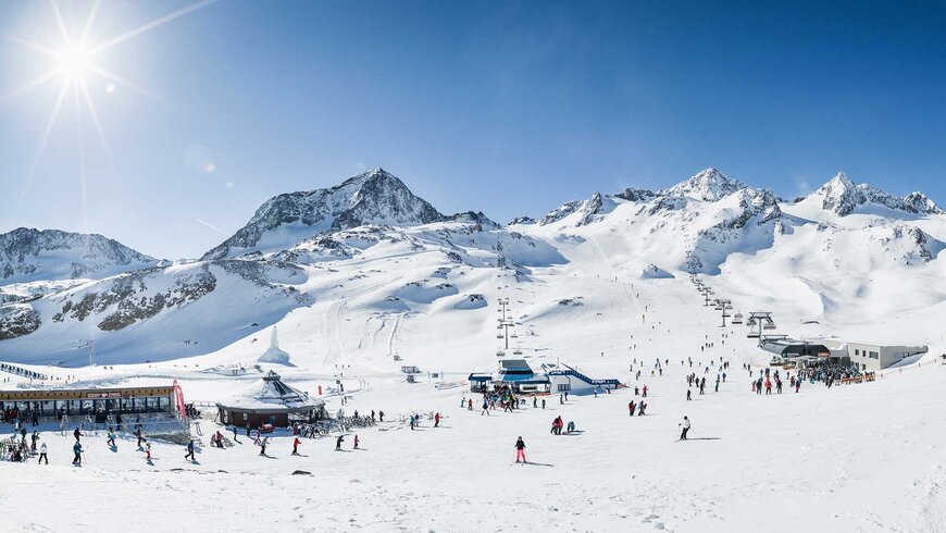 Skigebiet in Tirol mit schneebedeckten Bergen, Skiliften und zahlreichen Skifahrern unter strahlendem Sonnenschein.