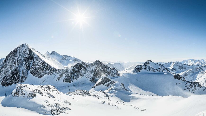 Panoramablick auf verschneite Bergspitzen im Stubaital mit blauem Himmel und strahlender Sonne.