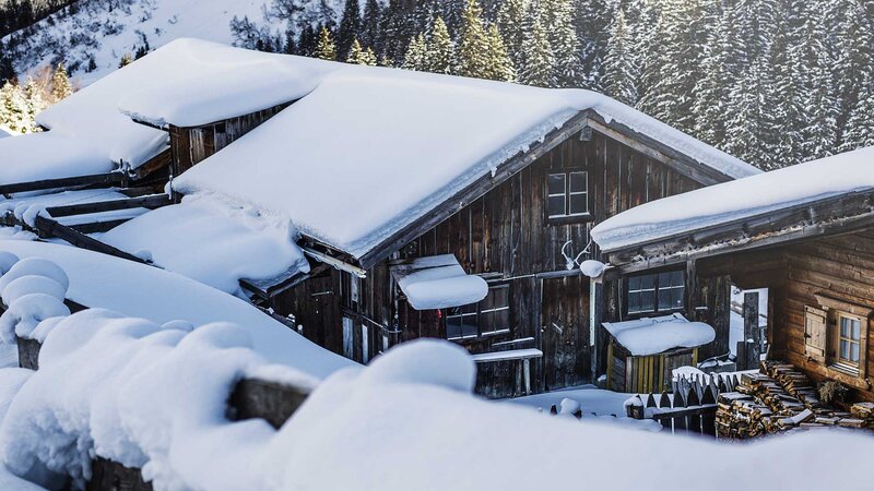 Verschneite Berghütte in Tirol umgeben von winterlicher Landschaft und dichten Wäldern.