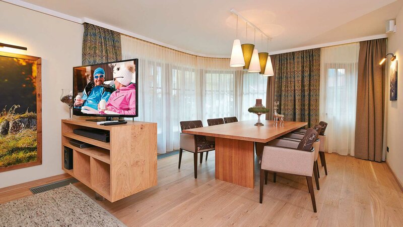 Einblick in den Ess- und Wohnbereich der Luxussuite mit großem Tisch und Flatscreen-TV