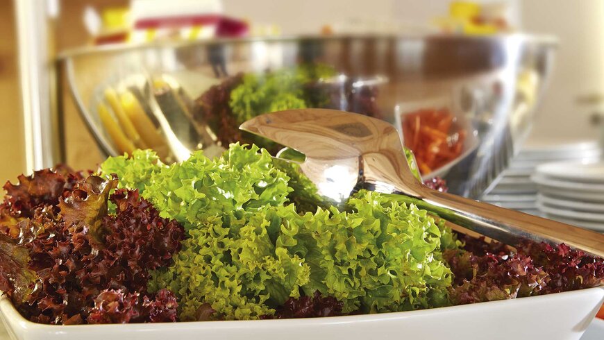 Frischer grüner und roter Blattsalat in einer Schüssel, bereit zum Servieren, mit einer Salatbesteck aus Holz.