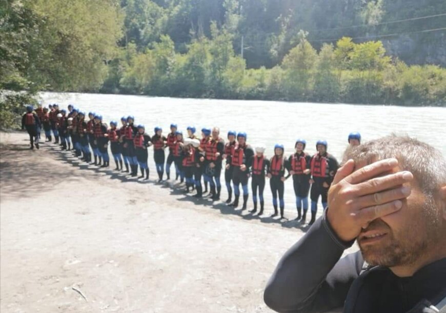 Eine große Gruppe von Abenteurern steht in Neoprenanzügen und Schwimmwesten am Ufer eines Flusses in Tirol, bereit für ein Rafting-Abenteuer. 