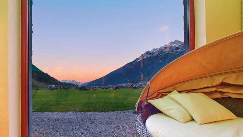 Ausblick aus dem Wellnessbereich des NatureSpas auf eine weitläufige Wiese und die Berge des Stubaitals