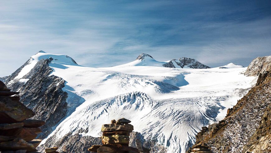 Schneebedeckte Gipfel der Alpen unter einem klaren blauen Himmel, mit Felsen im Vordergrund - perfekt für einen Aktivurlaub in Tirol.