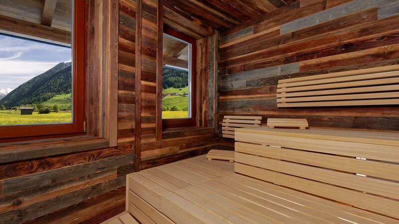 Ausschnitt der teilverglasten Finnischen Sauna mit Blick auf das unverbaute grün des Stubaitals