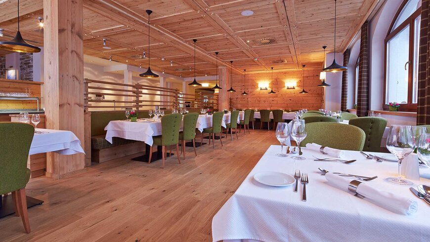 Elegantes Restaurant mit Holzwänden und -decke, grünen Polsterstühlen und weiß gedeckten Tischen, das eine gemütliche und warme Atmosphäre ausstrahlt.
