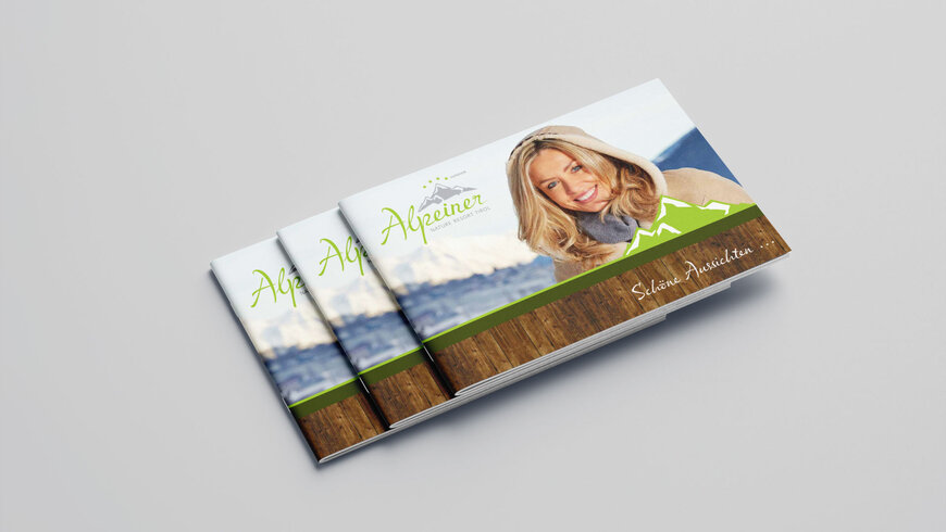 Drei gestapelte Broschüren des "Alpeiner Nature Resort Tirol" mit einem Bild einer lächelnden Frau in Winterkleidung auf dem Cover, vor einer Bergkulisse.