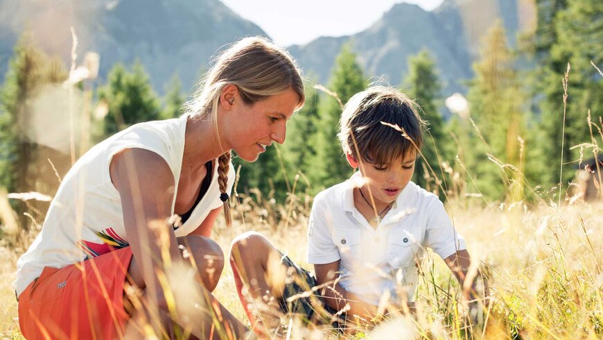 Eine Mutter und ihr Kind entdecken die Natur bei einem Sommerurlaub in Tirol, umgeben von hohen Bergen und üppigem Grün.