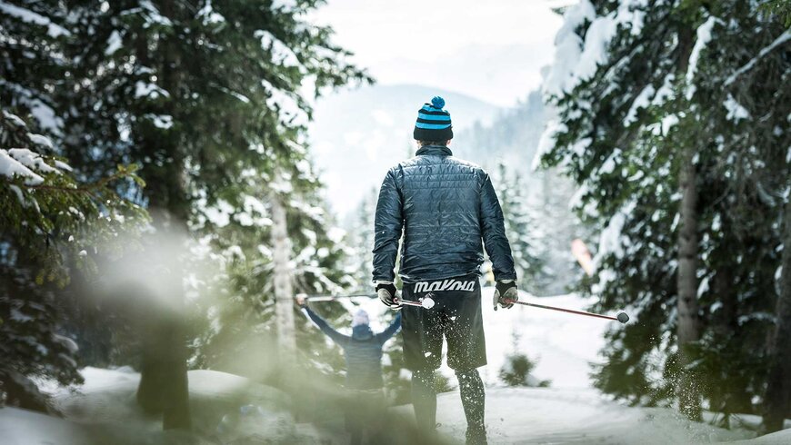 Ein Wanderer in warmer Winterkleidung mit Skistöcken in der Hand steht im verschneiten Wald im Aktivurlaub in Tirol.