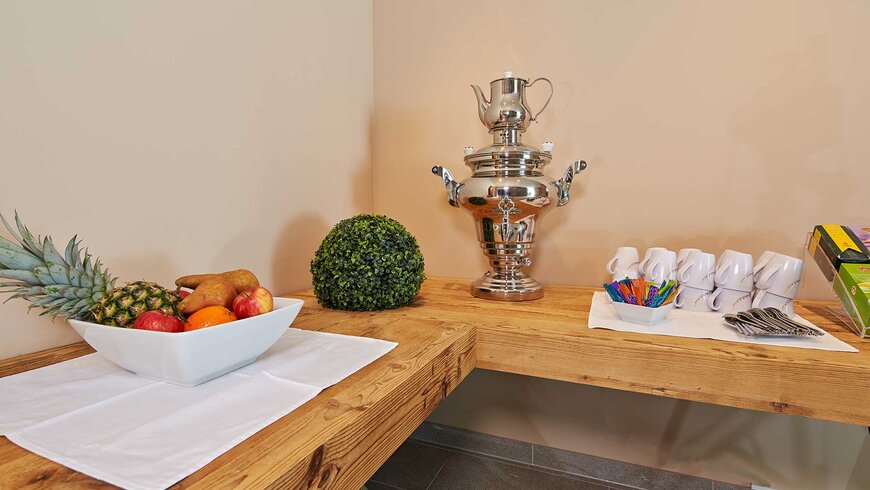 Ein gemütlicher Wellnessbereich im Stubaital mit einer rustikalen Holztheke, auf der eine Schale mit frischem Obst, ein dekorativer Buchsbaum und ein glänzender Teesamowar stehen, sowie eine Reihe von Tassen und Teelöffeln.