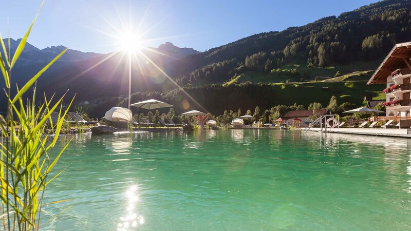 Ausschnitt des Naturbadeteichs inmitten der Berglandschaft bei Sonnenschein im Alpeiner Nature Resort in Neustift