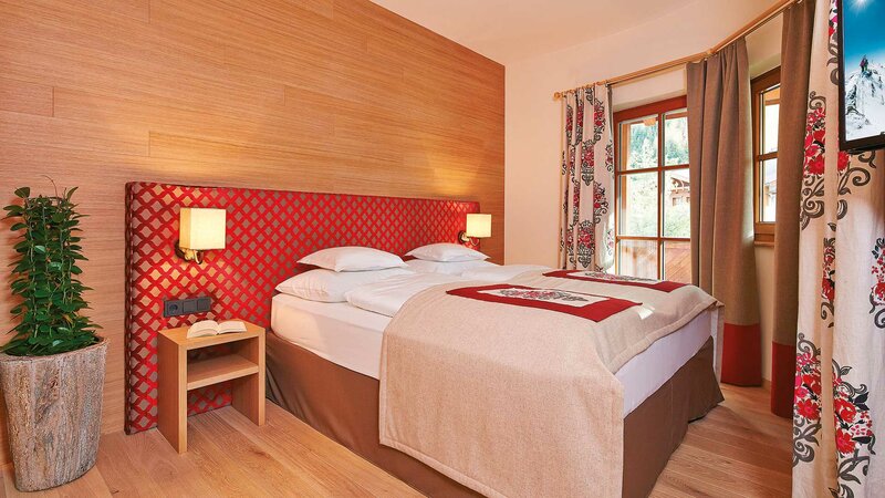 Einblick in das gemütliche Schlafzimmer der Luxussuite mit Doppelbett und Flatscreen-TV