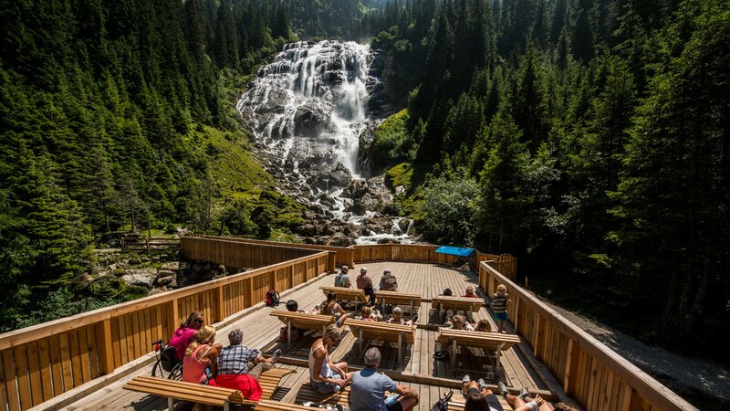 Eine Wandergruppe genießt während des Wanderurlaub in Tirol die Aussicht auf einen beeindruckenden Wasserfall in den Tiroler Alpen.