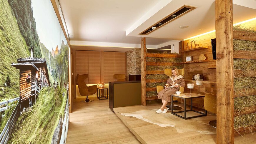 Entspannter Wellnessbereich im Stubaital mit Holzwänden, gemütlichen Sitzmöbeln und einer Frau in einem Bademantel.