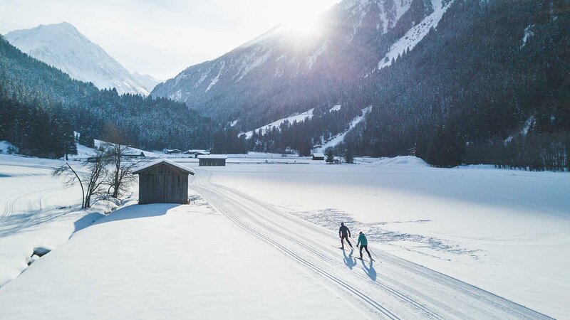 Zwei Langläufer gleiten über eine schneebedeckte Landschaft im Stubaital bei strahlendem Sonnenschein.