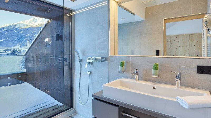 Einblick in das Bad des Superior Doppelzimmers mit offener Dusche und einer verglasten Wand mit Blick auf das Stubaital 