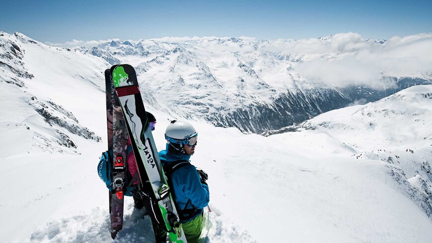Zwei Skifahrer mit Skiern auf dem Rücken genießen den atemberaubenden Blick auf die verschneiten Berge Tirols.