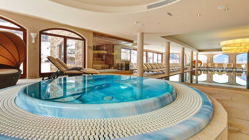Innenbereich eines Wellnesshotels im Stubaital mit einem großen Whirlpool und Liegestühlen neben einem beheizten Pool.