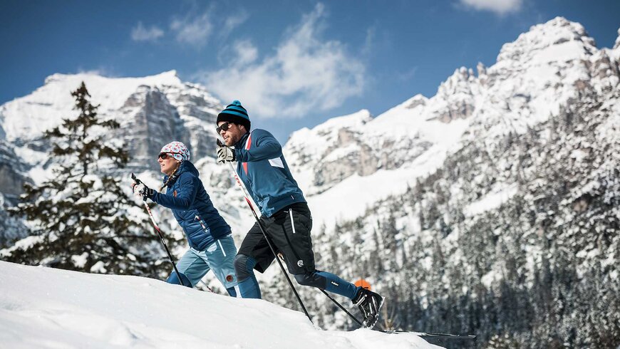 Zwei Menschen genießen den Aktivurlaub in Tirol beim Skilanglauf vor einer beeindruckenden verschneiten Bergkulisse.