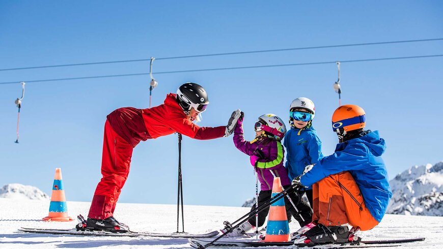Eine Familie genießt den Familienurlaub in Tirol beim Skifahren mit einem Skilehrer auf einer verschneiten Piste.