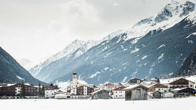 Ein verschneites Bergdorf in Tirol, umgeben von hohen, schneebedeckten Bergen.