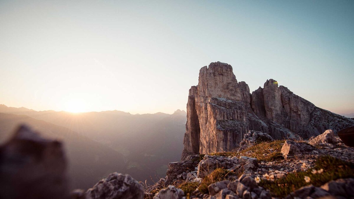 Ein spektakulärer Sonnenuntergang hinter einer imposanten Felsformation in den Tiroler Alpen, perfekt für Kletter- und Wanderabenteuer.