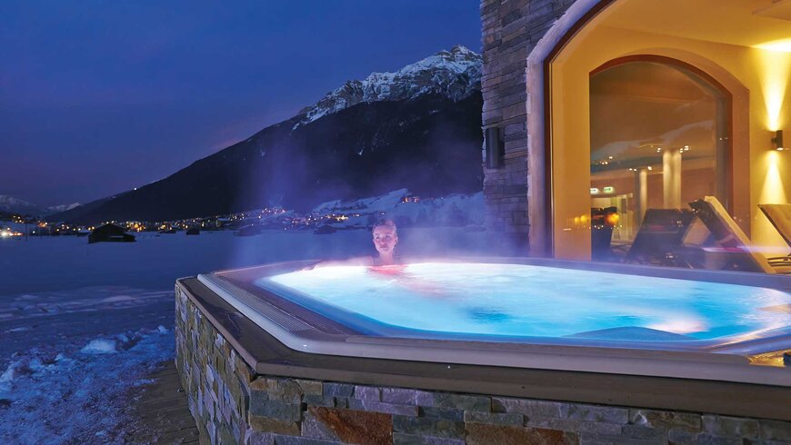 Ein Hotelgast in einem dampfenden Jacuzzi im schneebedeckten Außenbereich des Wellnessbereichs