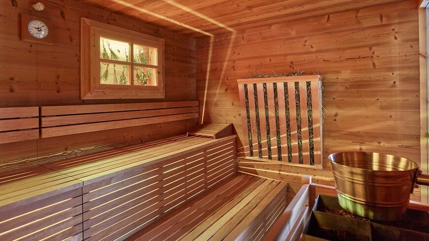 Eine gemütliche Holzsauna mit einem Fenster und einem Eimer für Aufgüsse in einem Wellnesshotel im Stubaital.