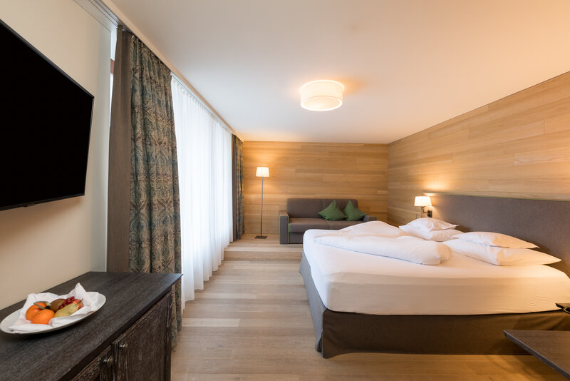 Ein modernes Hotelzimmer mit einem großen Bett, einem Fernseher, einer gemütlichen Sitzecke und einem Teller mit frischem Obst.