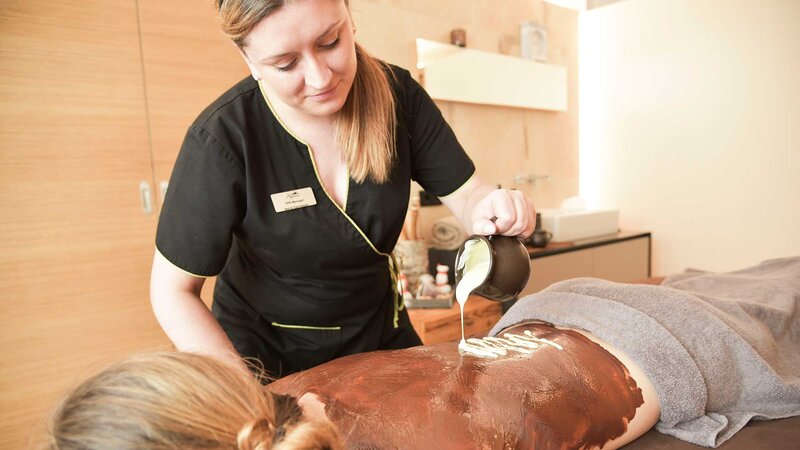 Eine Kosmetikerin bei der Körperbehandlung an einem vor ihr liegenden Hotelgast im Nature Spa