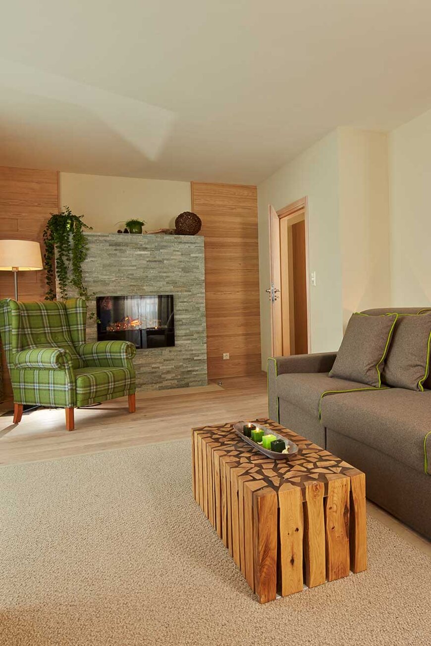 Gemütliches Wohnzimmer im 4 Sterne Hotel im Stubaital mit grün kariertem Sessel, modernem Kamin und rustikalem Holztisch.