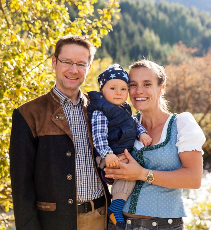 Eine kleine Familien mit Mutter, Vater und Kind in traditioneller Kleidung lachen in die Kamera.