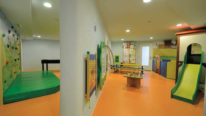 Spielzimmer in einem Kinderhotel in Tirol mit Kletterwand, Spieltisch und Rutsche.