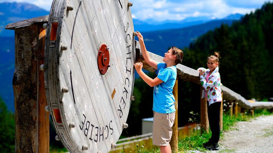 Kinder spielen an einer großen Holzscheibe in den malerischen Bergen Tirols während eines Aktivurlaubs.