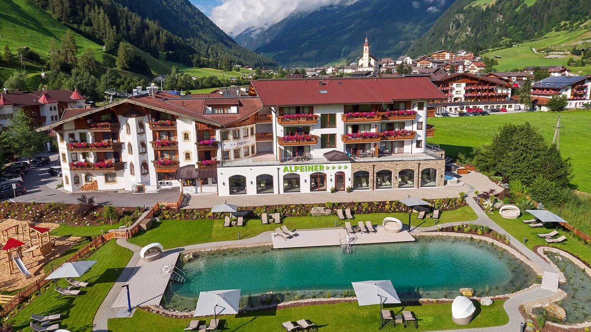 Das Hotel Alpeiner in Tirol mit Blick auf die Alpen, grüne Wiesen und einem idyllischen Außenpool.