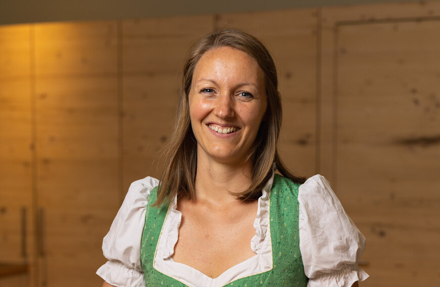 Eine braunhaarige Frau in traditioneller grüner Tracht lächelt freundlich in die Kamera.