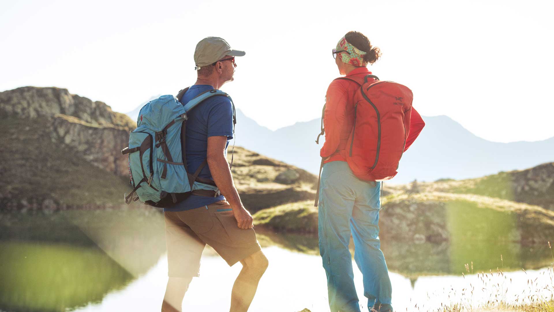 Zwei Wanderer mit Rucksäcken genießen während ihres Aktivurlaubs in Tirol die Aussicht auf eine malerische Berglandschaft.