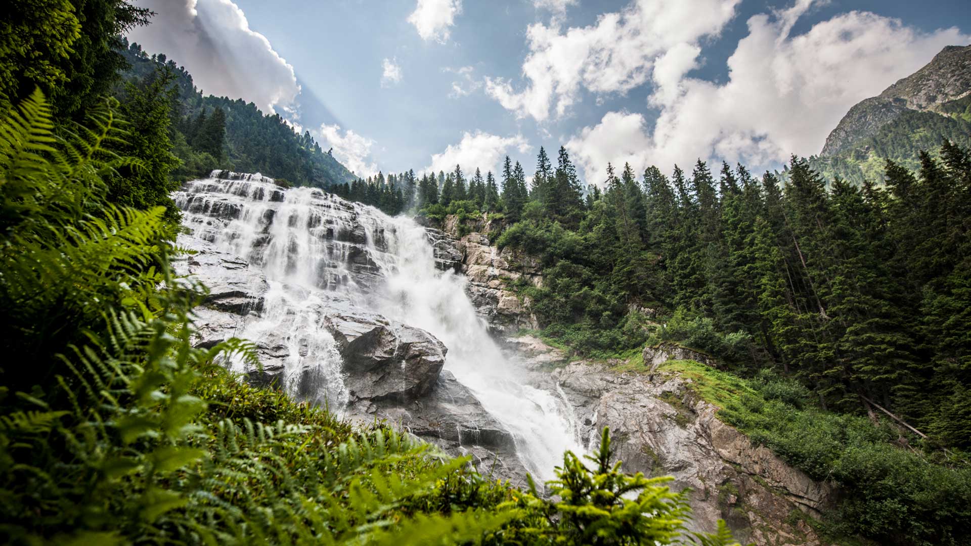 Ein beeindruckender Wasserfall inmitten einer üppigen grünen Landschaft und hohen Bäumen, ideal für einen Wanderurlaub in Tirol.